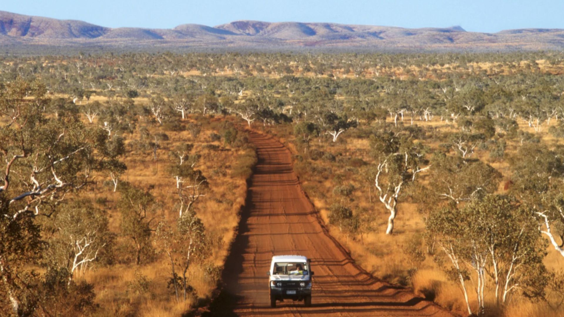 White 4WD vehicle driving along remote red dirt road in the Australian outback, highlighting rural connectivity and emergency response readiness.