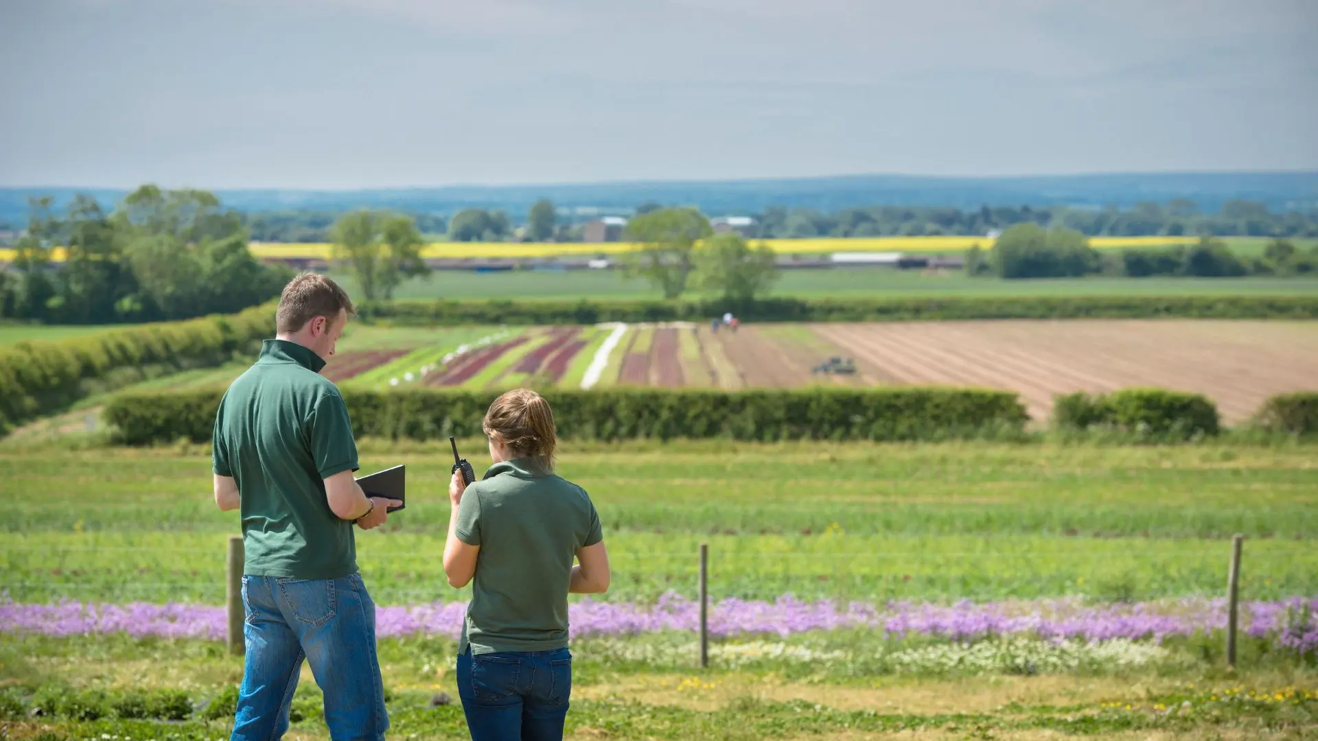 Two agricultural workers using a tablet and radio to monitor farming operations in a rural field